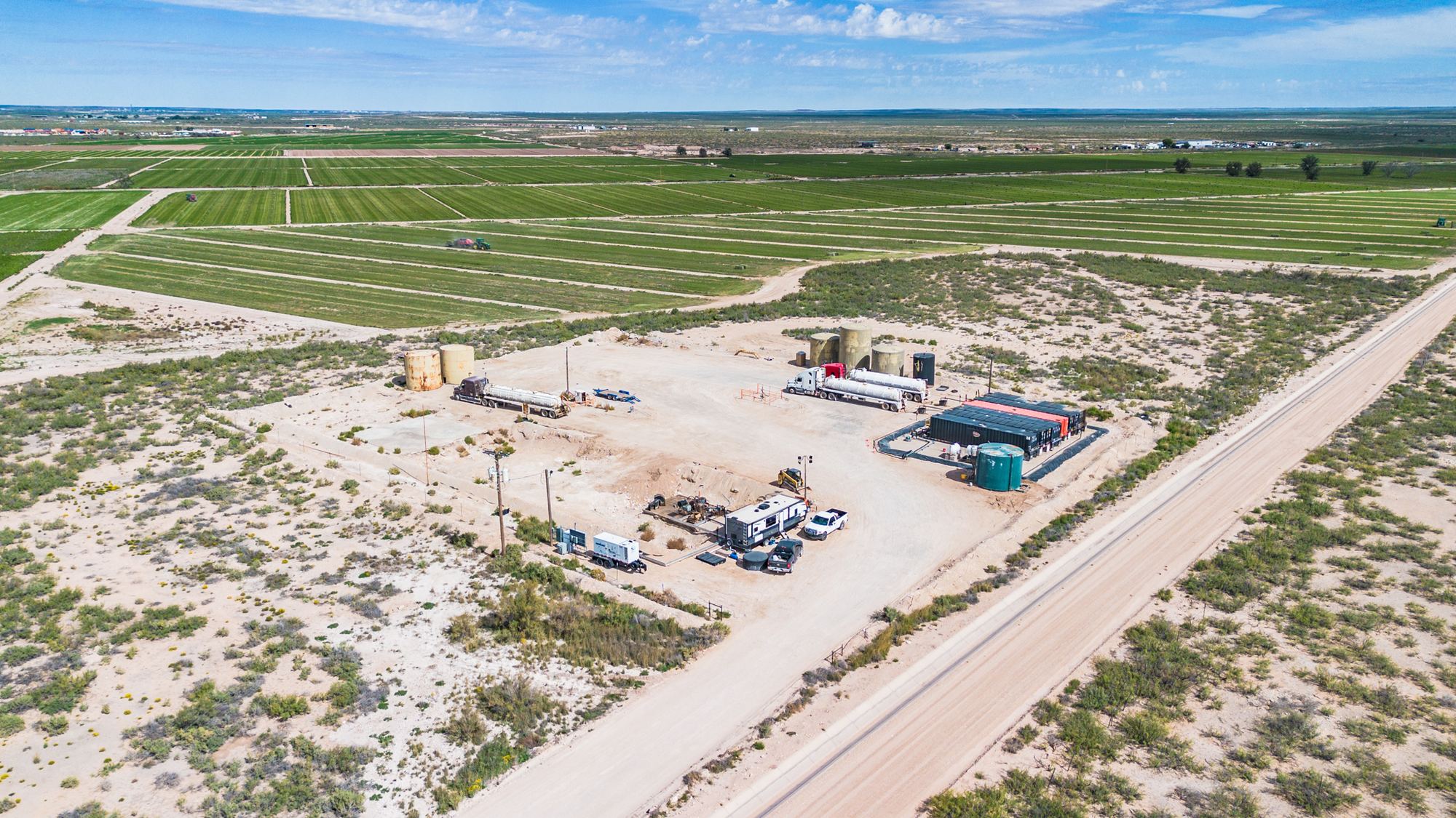 Aerial view of the Buckeye Saltwater Disposal pad beside a caliche road, with tank batteries, haul trucks and irrigated fields beyond