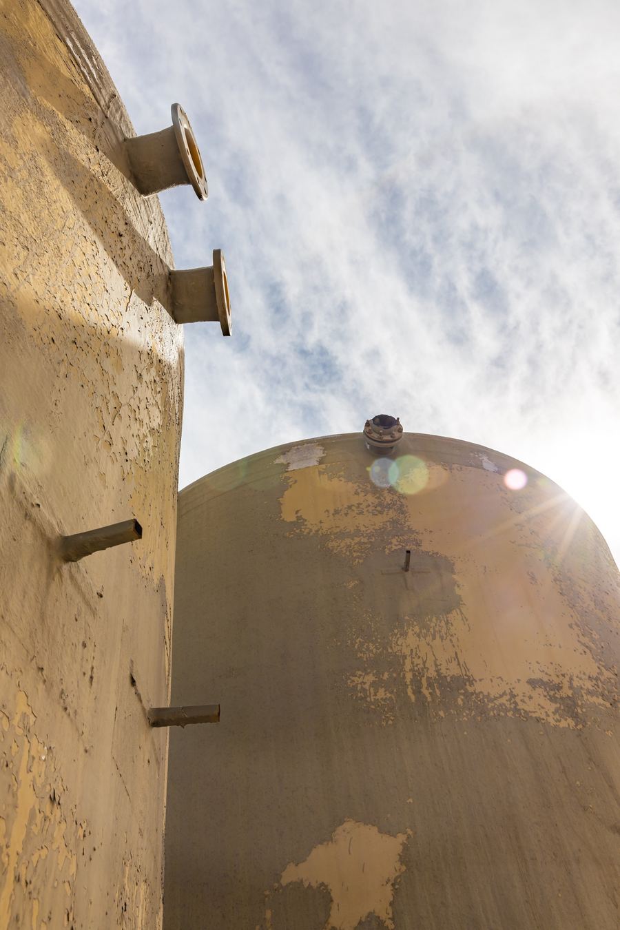 Weathered storage tanks against a bright desert sky
