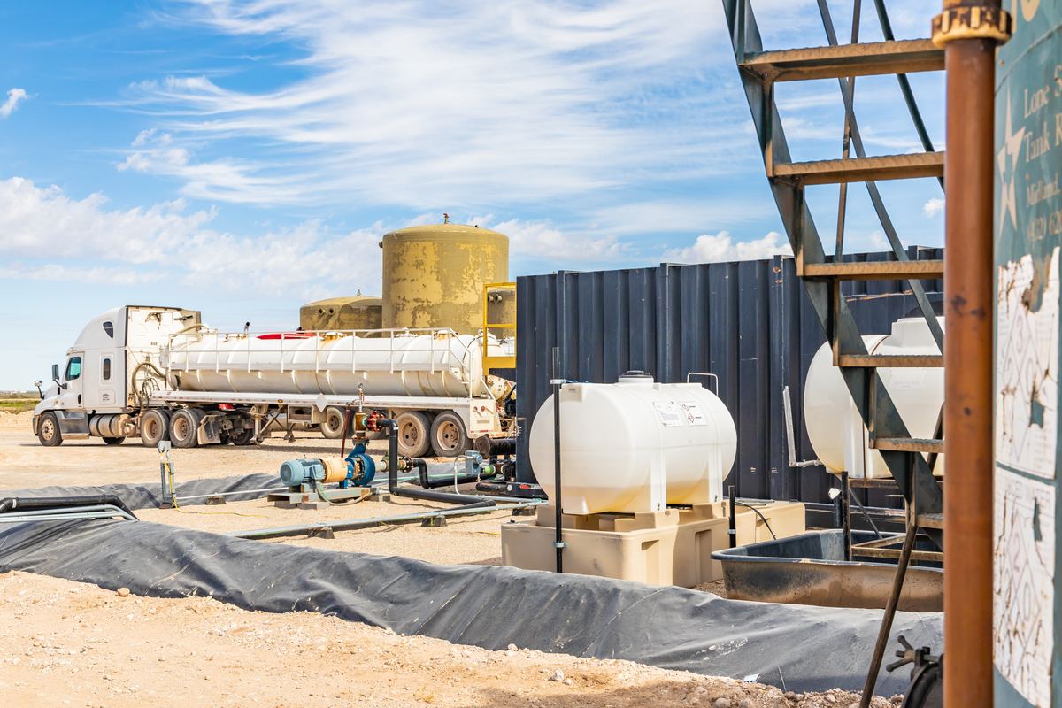 A vacuum truck parked at the offload area beside tanks and a lined containment berm